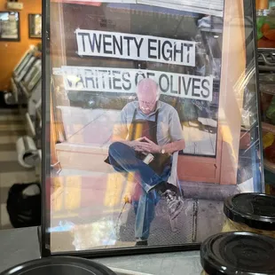 a picture of a man sitting on a bench with a jar of olives in front of him