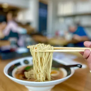a person holding chopsticks over a bowl of ramen