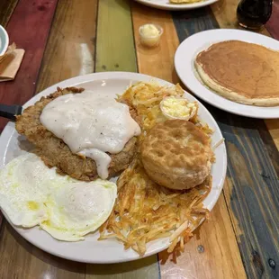 Chicken fried steak with hash browns biscuits eggs and pancake.