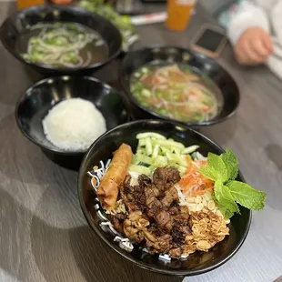 On left broth &amp; side of jasmine rice, on right steak phó, in front grilled pork &amp; egg roll vermicelli