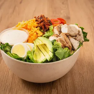 chicken, lettuce, tomatoes, avocado, and dressing in a bowl