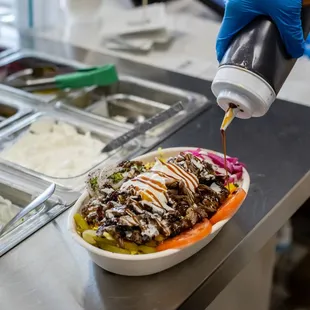 a person in a blue glove pouring ketchup onto a bowl of food
