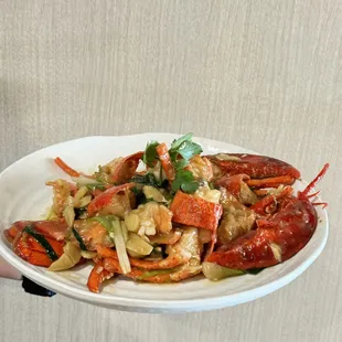 The lobster on the plate has a bright red color, paired with vegetables and garnished with cilantro, which is very appetizing.