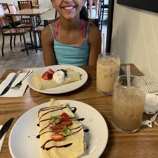 a young girl sitting at a table with a plate of food