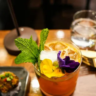 a glass of cocktail with a flower garnish