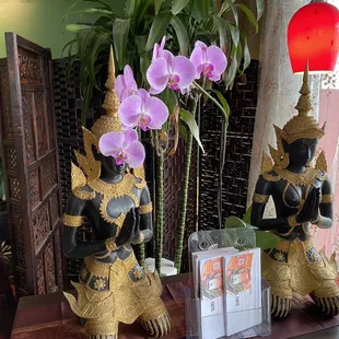 a pair of statues with orchids in the background