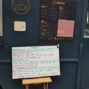 a menu written on a board in front of a food truck