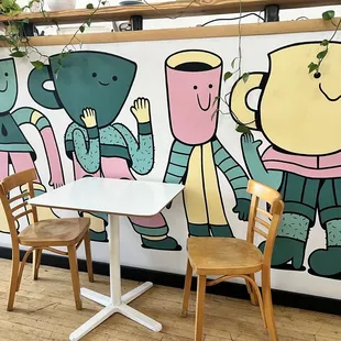 a table and chairs in front of a mural