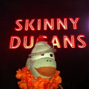 a sock monkey with a neon sign in the background