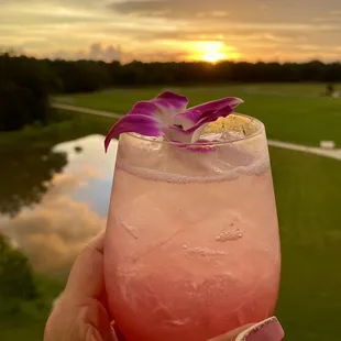 a hand holding a pink drink with a purple flower