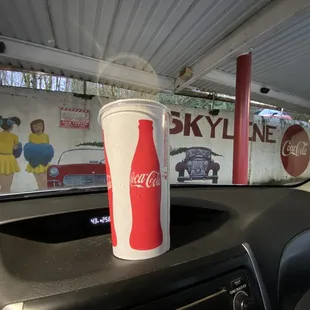 a coca cola cup on the dashboard of a car