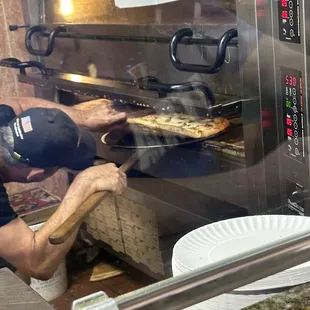 Pizzaiola checking on the pizza crust just before serving