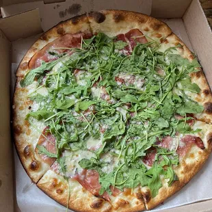 a pizza in a box with greens on top