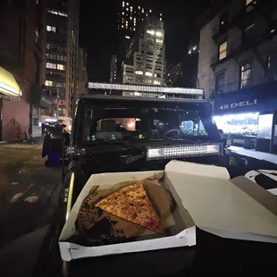 a pizza in a box on the hood of a pickup truck