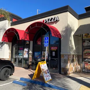 a pizza place with a sign in front of it