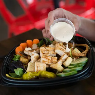 a person pouring dressing over a salad