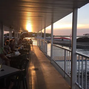 people sitting at tables on a deck overlooking the water