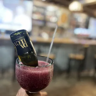 a hand holding a wine glass with a wine bottle in it