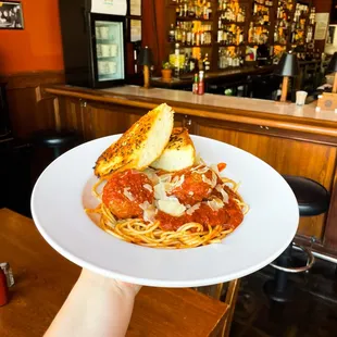 a person holding a plate of spaghetti and bread