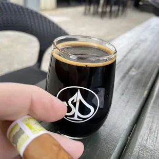 a hand holding a cigar and a glass of coffee