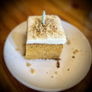 a slice of carrot cake with a single candle on top