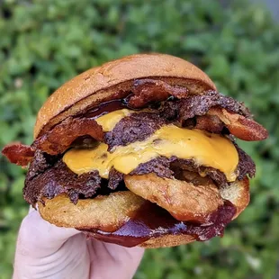 a hand holding a bacon and cheese sandwich