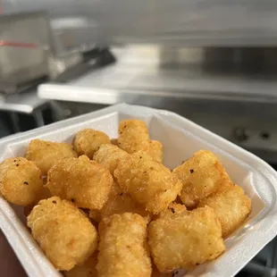 a hand holding a container of fried tater tots