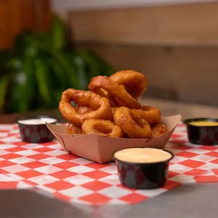 a basket of onion rings and dipping sauces