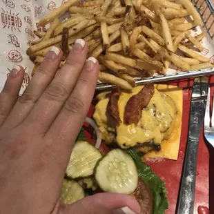 a person's hand grabbing a piece of cheeseburger and french fries