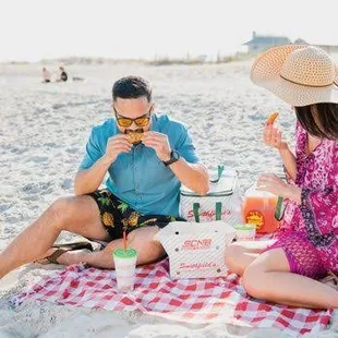 ws a man and a woman sitting on the beach eating a sandwich