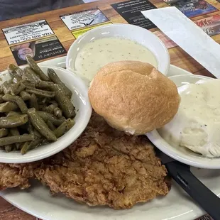 Pork tenderloin dinner with gravy on the side, mashed potatoes and green beans with a roll of