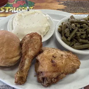 Two pieces fried chicken dark with mashed potatoes, green beans and a roll
