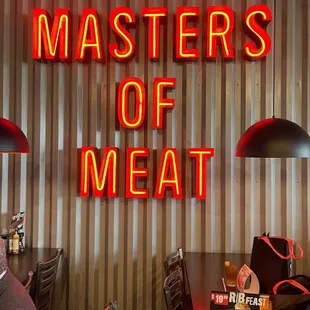 a man sitting at a table in front of a neon sign that says masters of meat