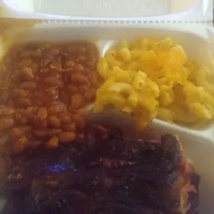 a white styrofoam container filled with meat, beans, and macaroni and cheese