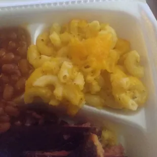 a white styrofoam container filled with macaroni and cheese and beans