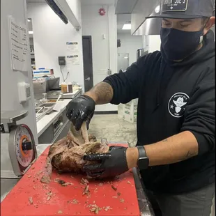 ows a man wearing a mask and gloves cutting meat