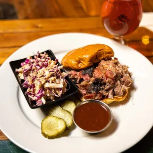 a plate of pulled pork, coleslaw, pickles, and a beer