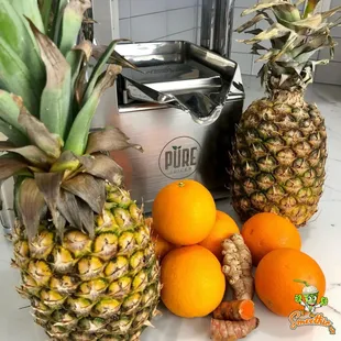 a pineapple, oranges, and a juicer