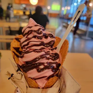 Strawberry plant based soft serve with chocolate syrup in a freshly made waffle cone