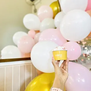 a person holding a cupcake in front of balloons