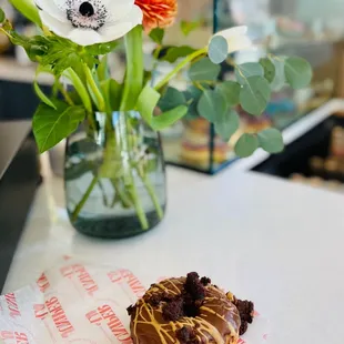 a donut on a table with a vase of flowers in the background