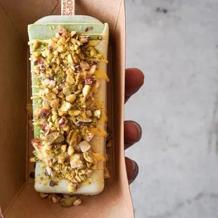 Pistachio pop half dipped in white chocolate topped with chopped pistachio.