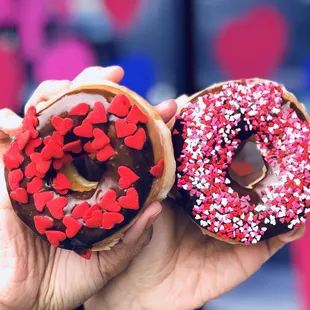 a hand holding a chocolate donut with sprinkles