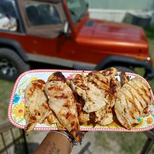 a person holding a plate of grilled chicken
