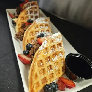 a plate of waffles with fruit and powdered sugar