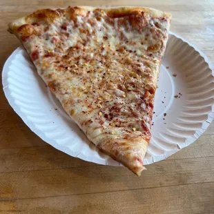 A slice of Cheese Pizza by Slice. A little crushed red pepper added.