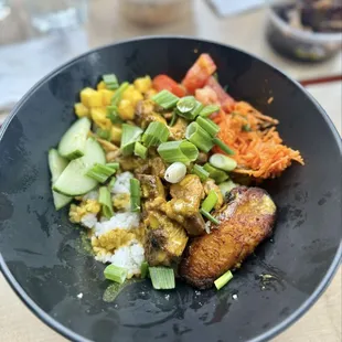 Sizzlin&apos; Someting bowl with curry chicken, ginger carrot slaw, marinated tomato, cucumber, fried plantain, mango, and green onion