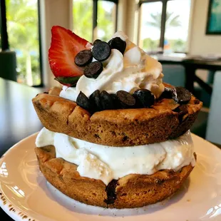 Hershey's Vanilla Ice Cream between Two Warm Chocolate Chip Cookies topped with Whipped Cream, Chocolate chips, and a Strawberry.