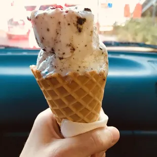 Two scoops of vegan cookies and cream in a waffle cone to go (one scoop is half eaten in this photo)