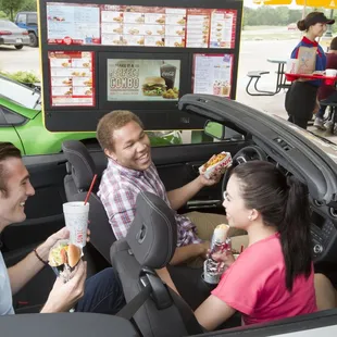 three people eating hot dogs in a car